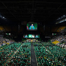 A graduation ceremony, with the graduates in green robes facing the stage.